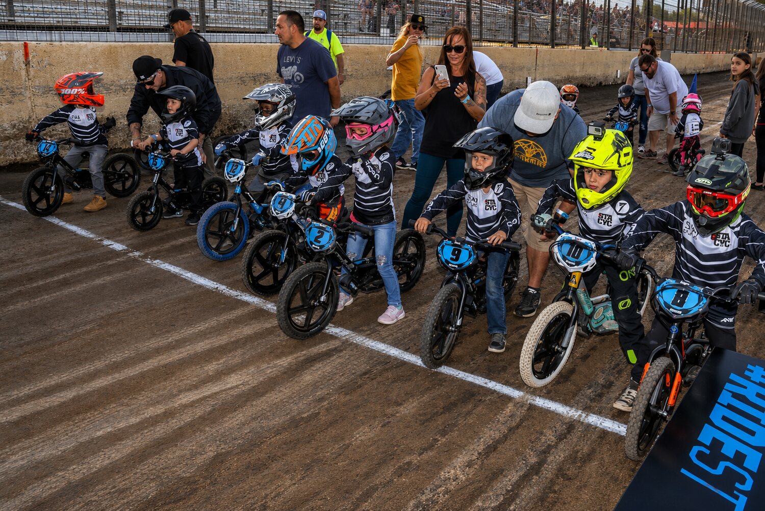 A line of young children on StaCyc electric balance bikes at the start with their parents